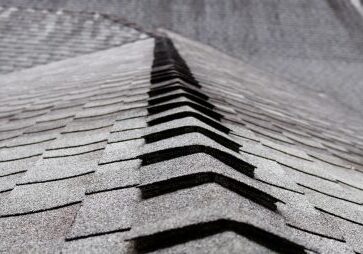 Close-up view of asphalt roof shingles arranged in a neat, overlapping pattern along the ridge of a roof.
