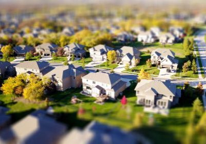 Aerial view of a suburban neighborhood with numerous single-family homes, green lawns, trees, and curved roads on a sunny day—can you spot which ones might be asking, "Do You Need a New Roof?.